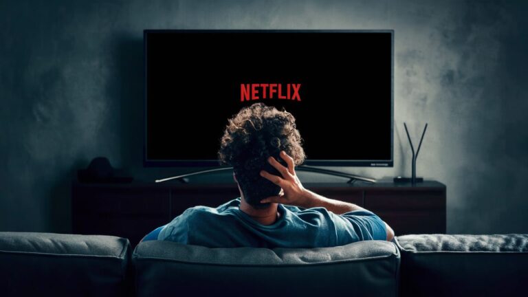 A person sitting on a couch and watching a smart TV screen displaying Netflix